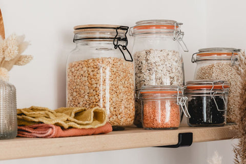 Jars of colourful dried beans, lentils and oats on a wooden shelf with natural linen cleaning cloths.